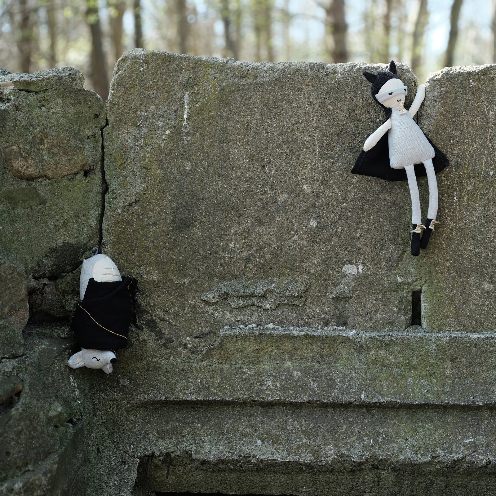 A toy doll dressed as a superhero with a black cape and white costume, perched on a stone surface.